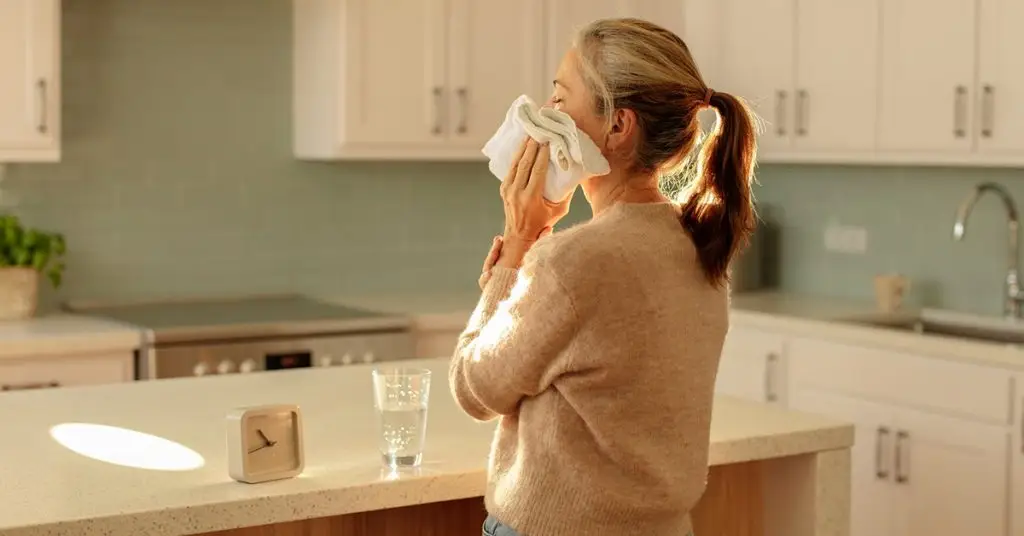 Woman at her kitchen counter holding a cloth to her cheek after a weekend tooth injury.